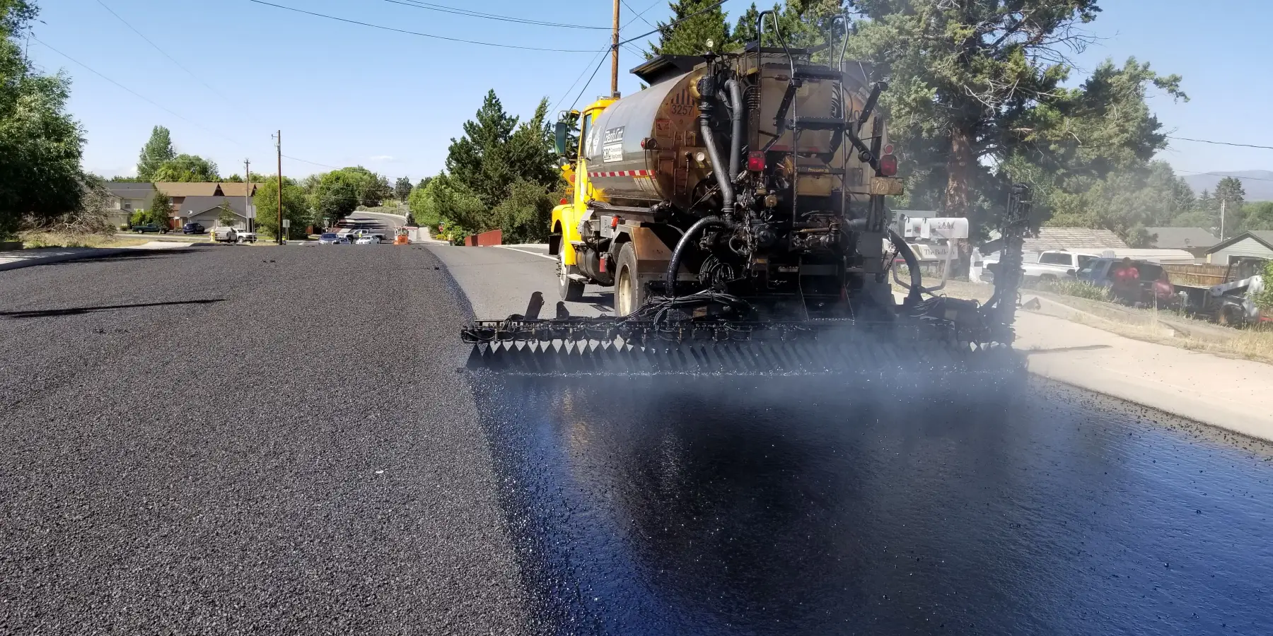A distributor truck spraying emulsion beside a freshly paved lane on a residential street