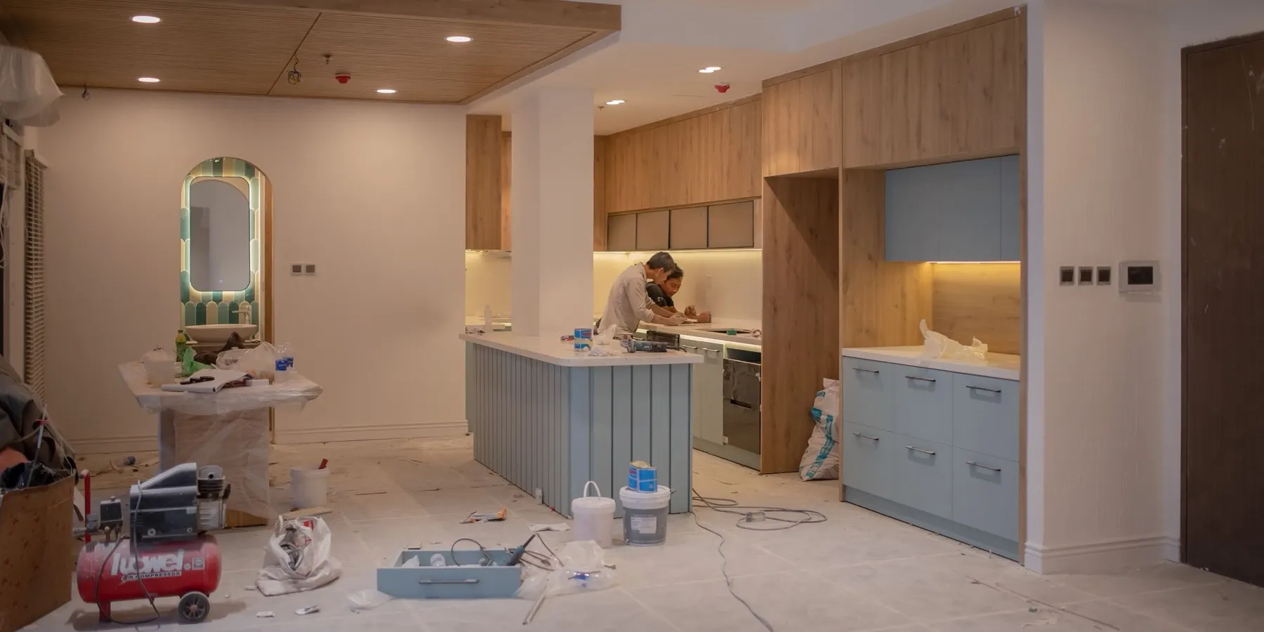Two workers fitting pale blue and oak cabinets in a kitchen still under renovation