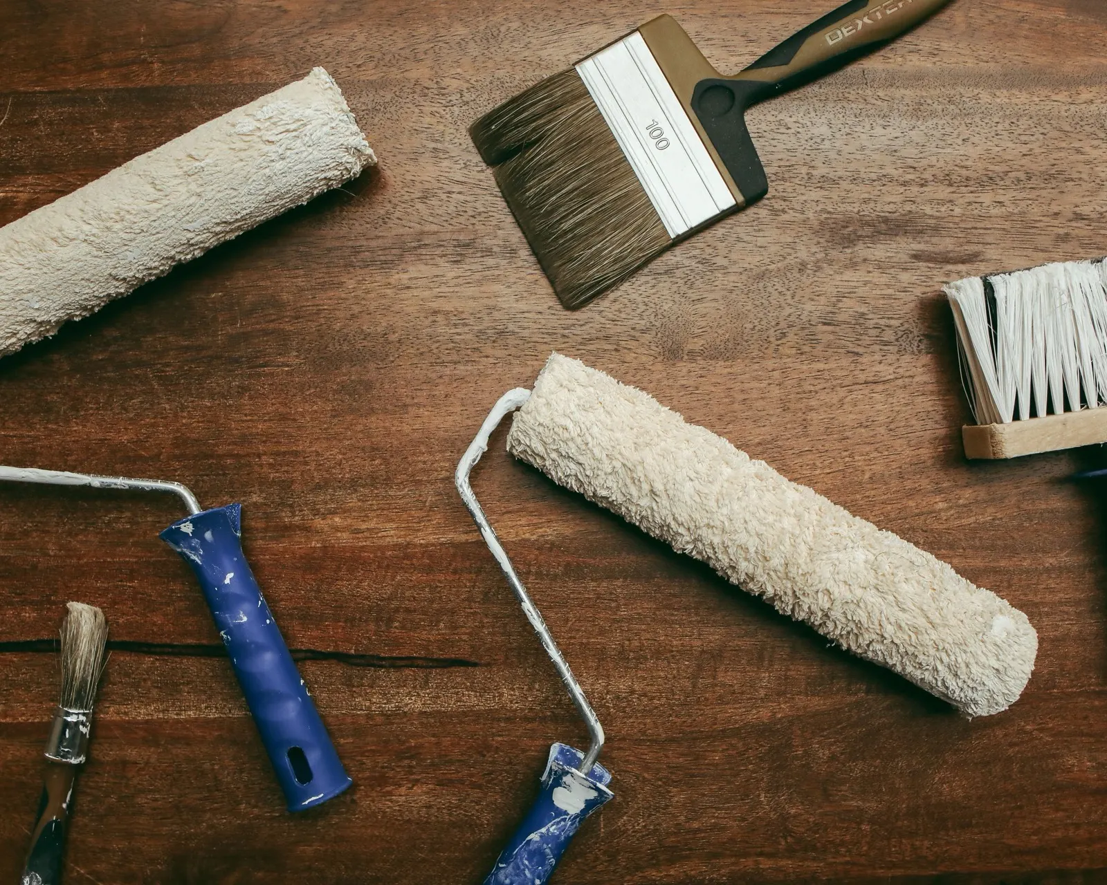 Paint rollers and brushes laid out on a wooden surface