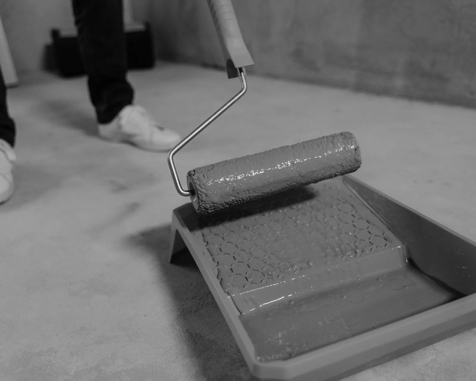 Roller on an extension pole beside a paint tray and cutting-in brush