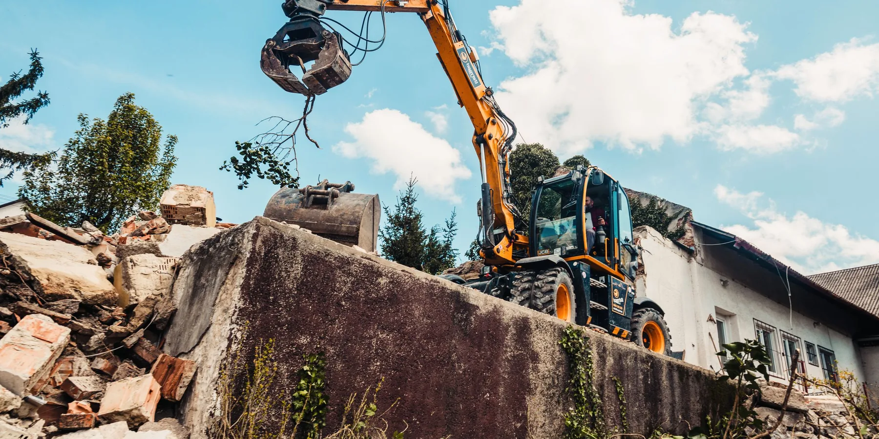 An excavator grapple lifting a broken concrete section clear