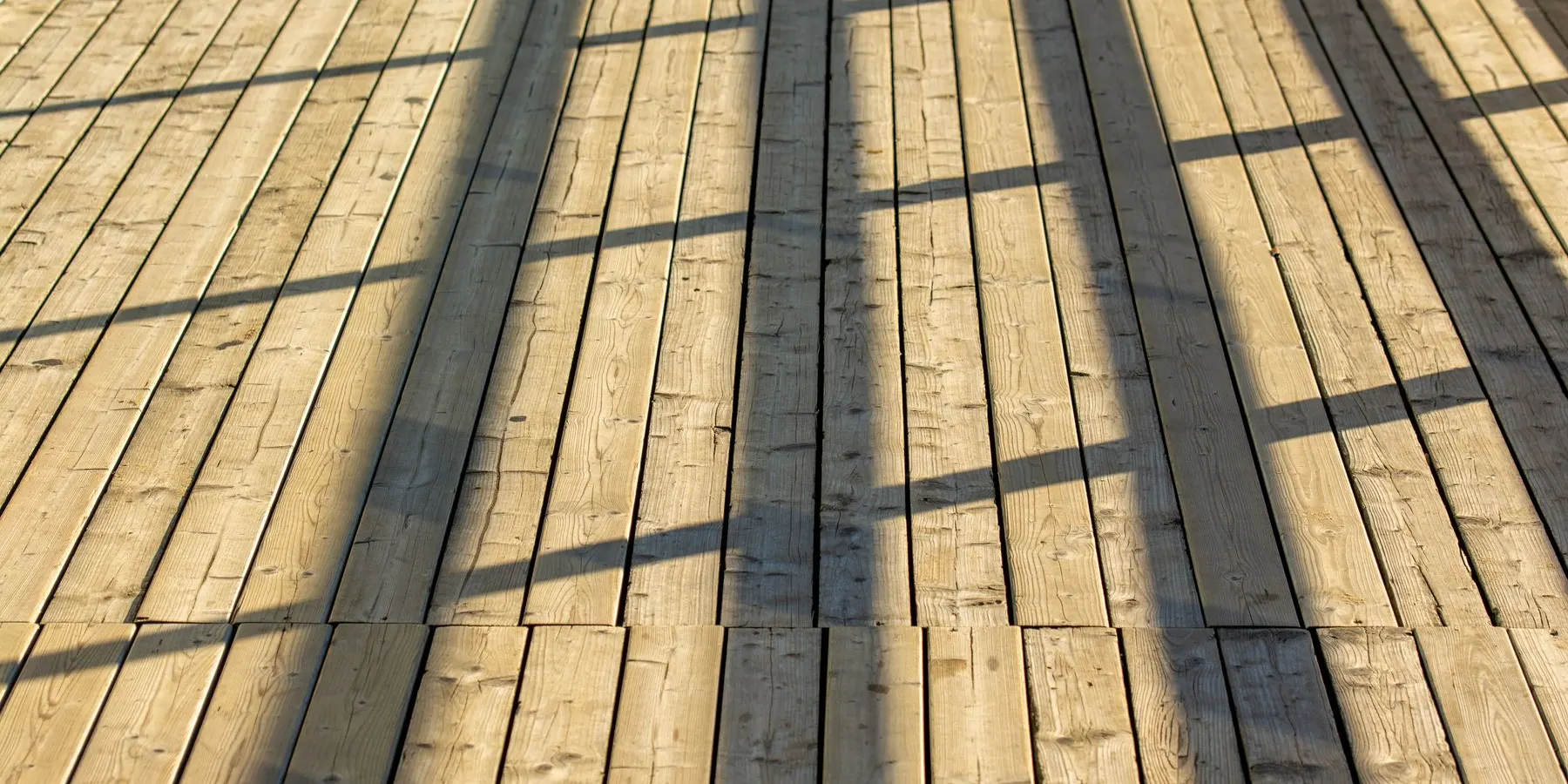 Sunlit wooden deck boards with the shadow of a railing falling across them