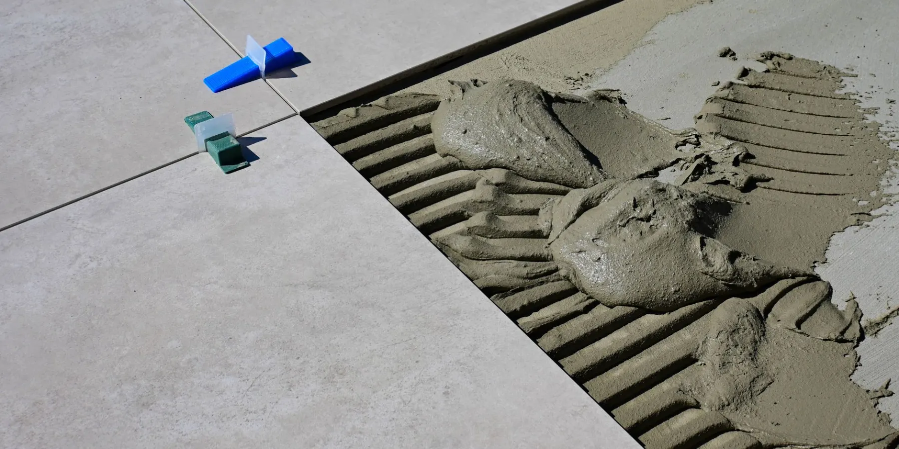 Cement mortar spread on a floor next to newly laid tile and leveling spacers