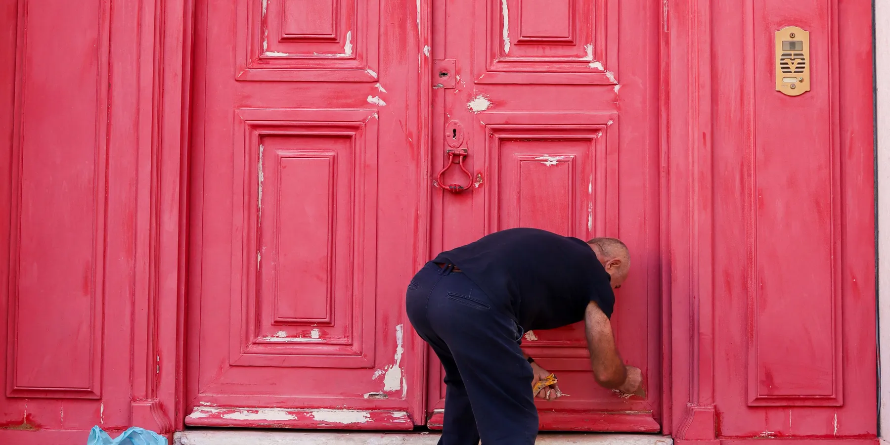 A man working on the worn red paneled double door of a historic building