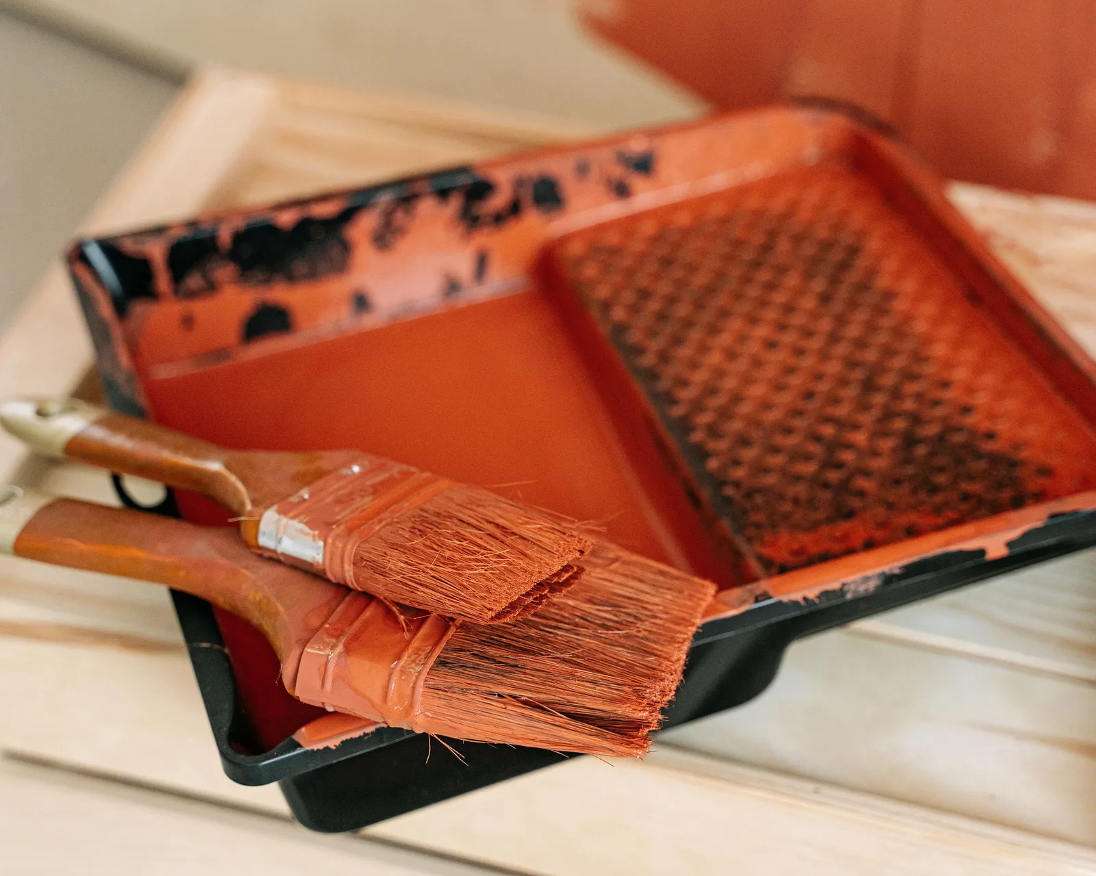 Two paintbrushes resting on a paint tray with a roller grid