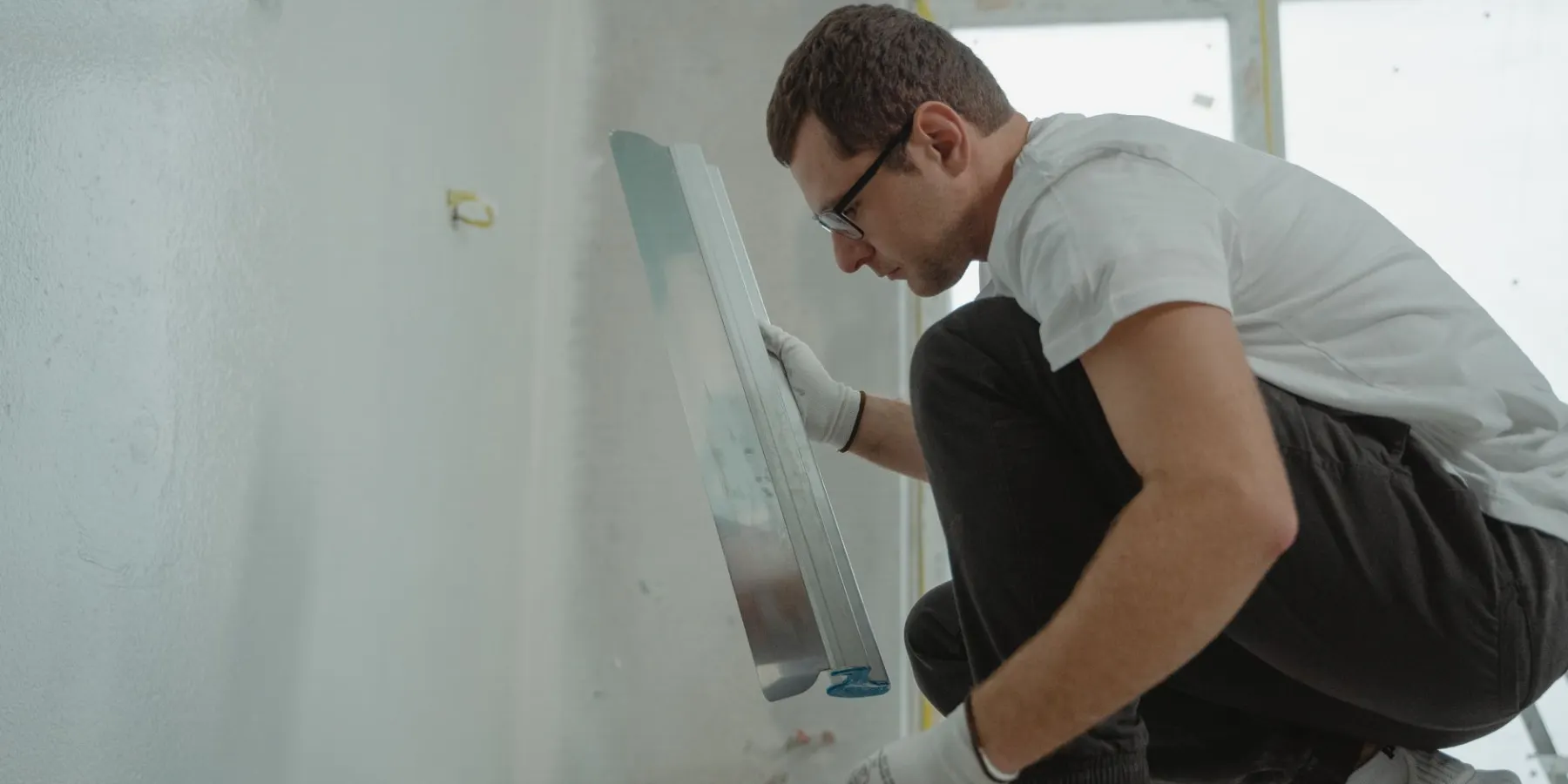 Drywall finisher holding a wide finishing knife against a skim-coated wall