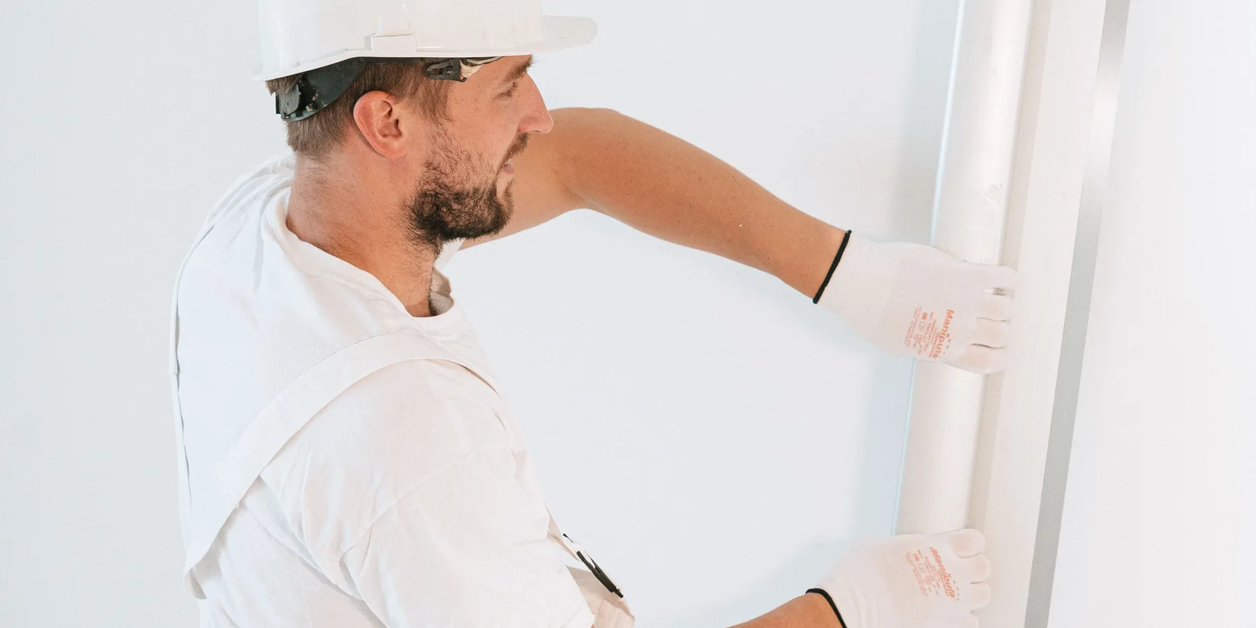Worker in gloves and helmet hanging a sheet of drywall
