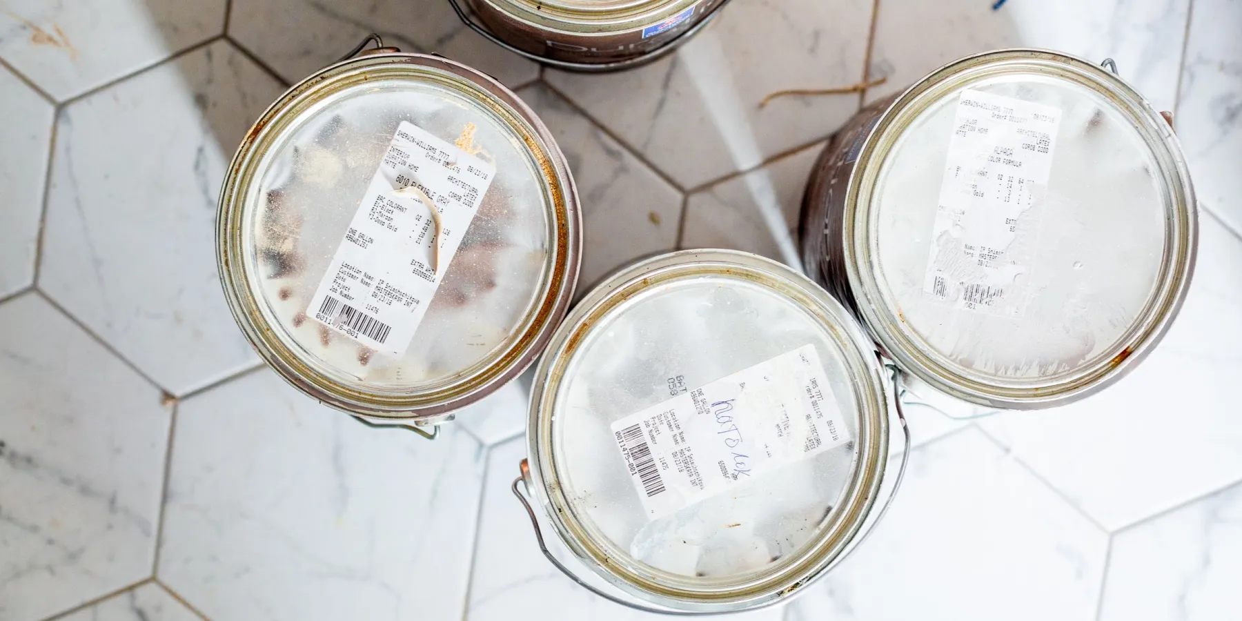 Three gallon paint cans seen from above on a white hexagonal tile floor