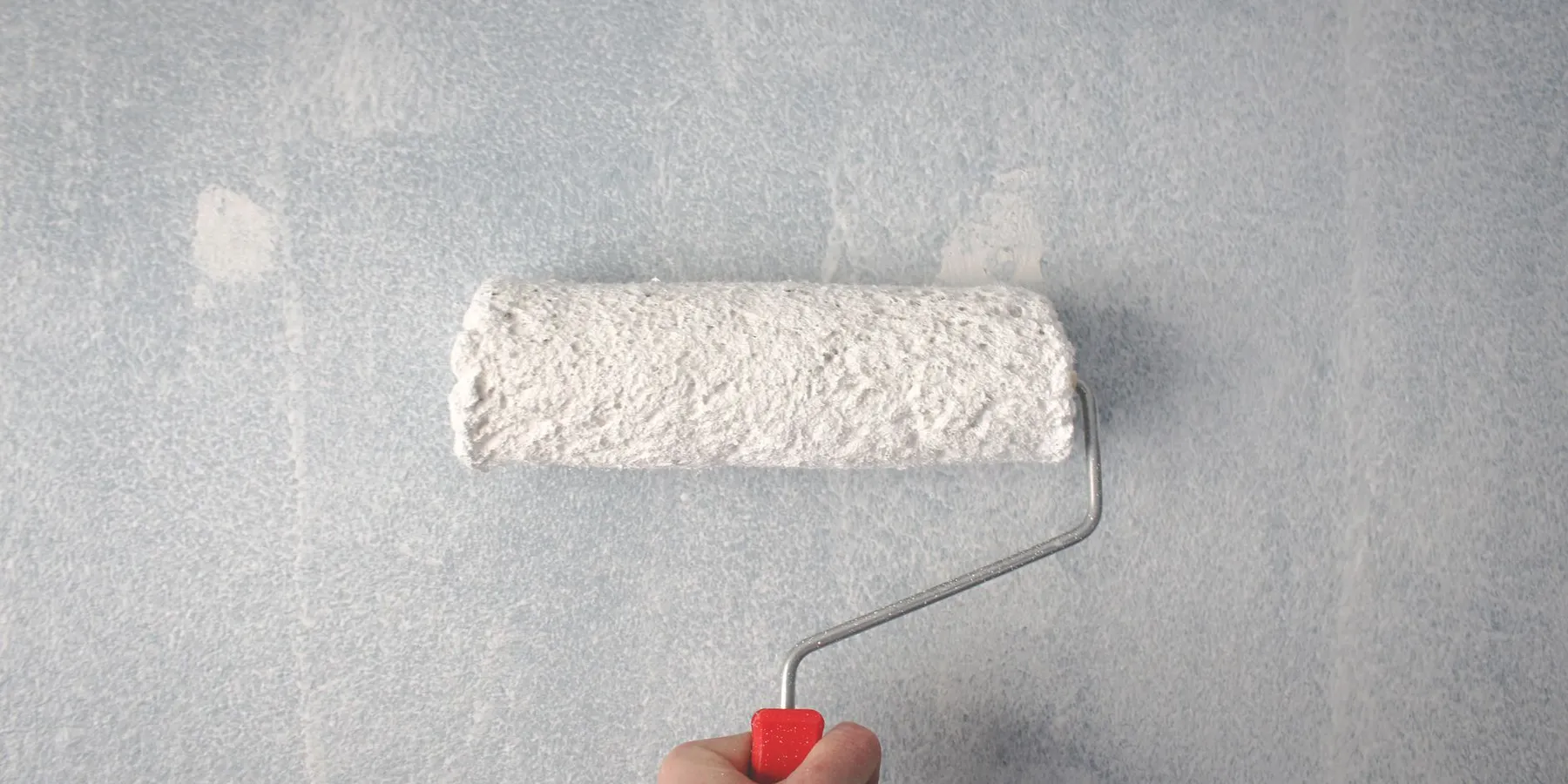 Paint roller applying white paint to a wall