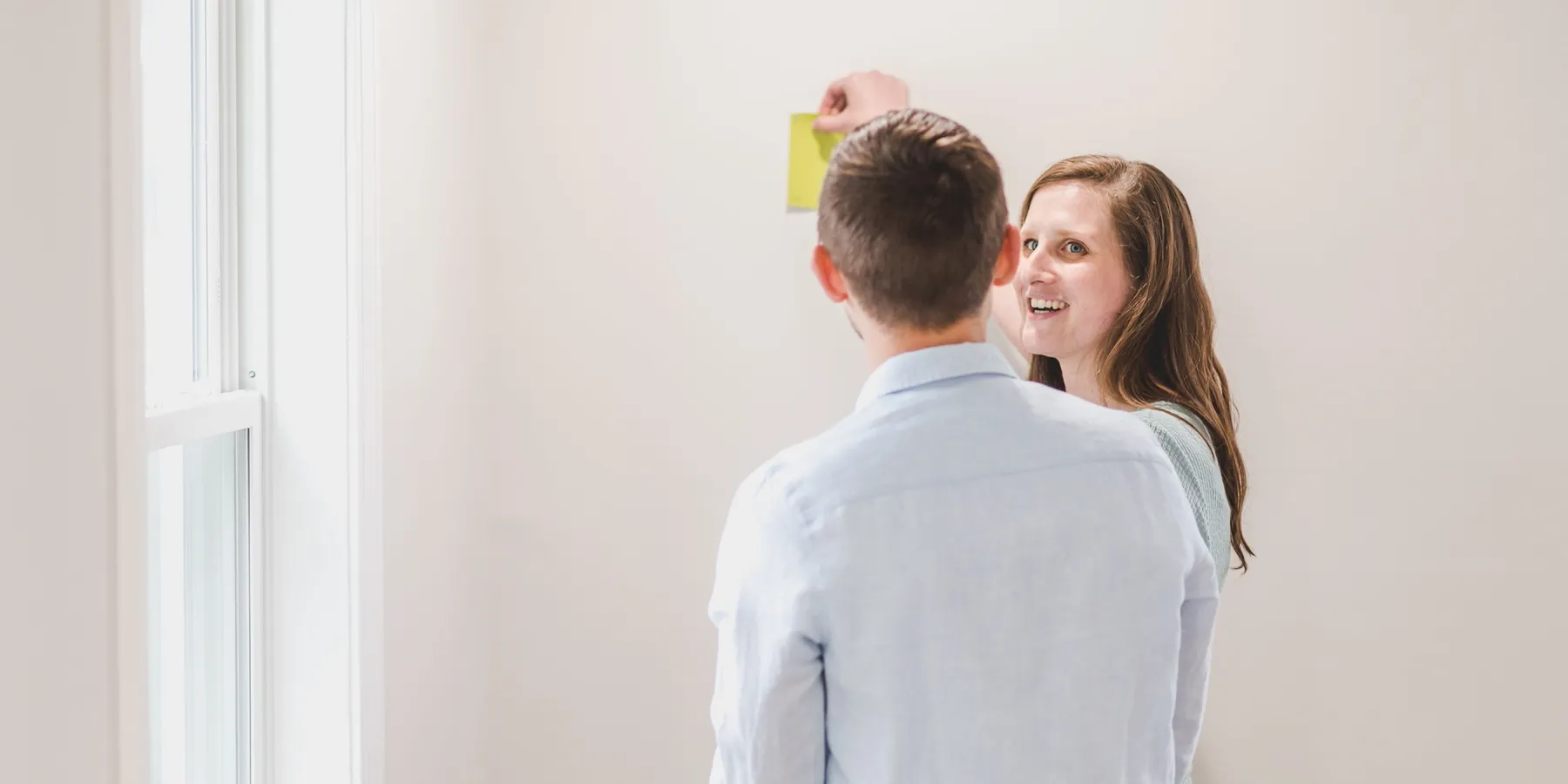 Two people holding a paint colour swatch against a wall