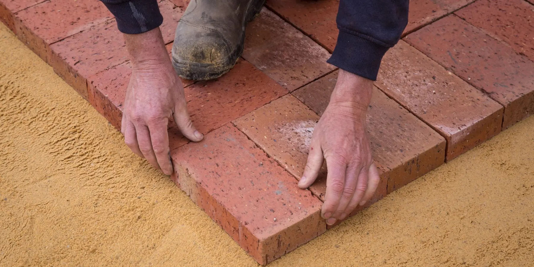Hands setting clay pavers on a screeded sand bed