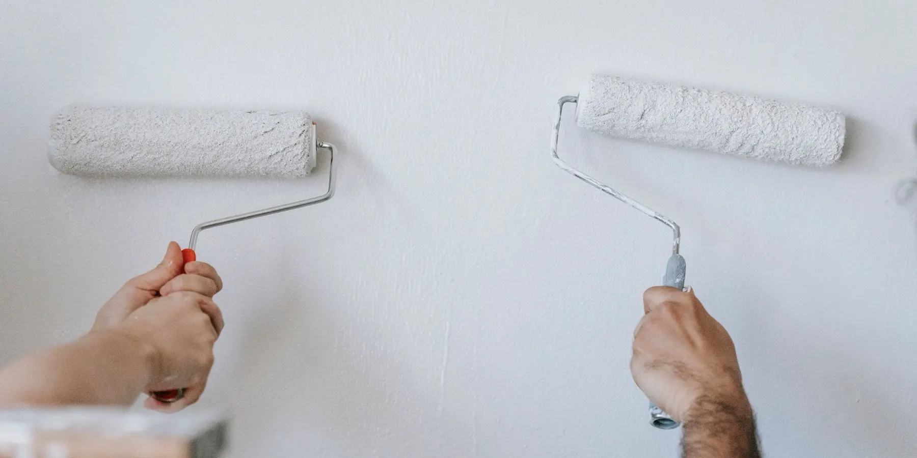 Two paint rollers applying white primer to a wall