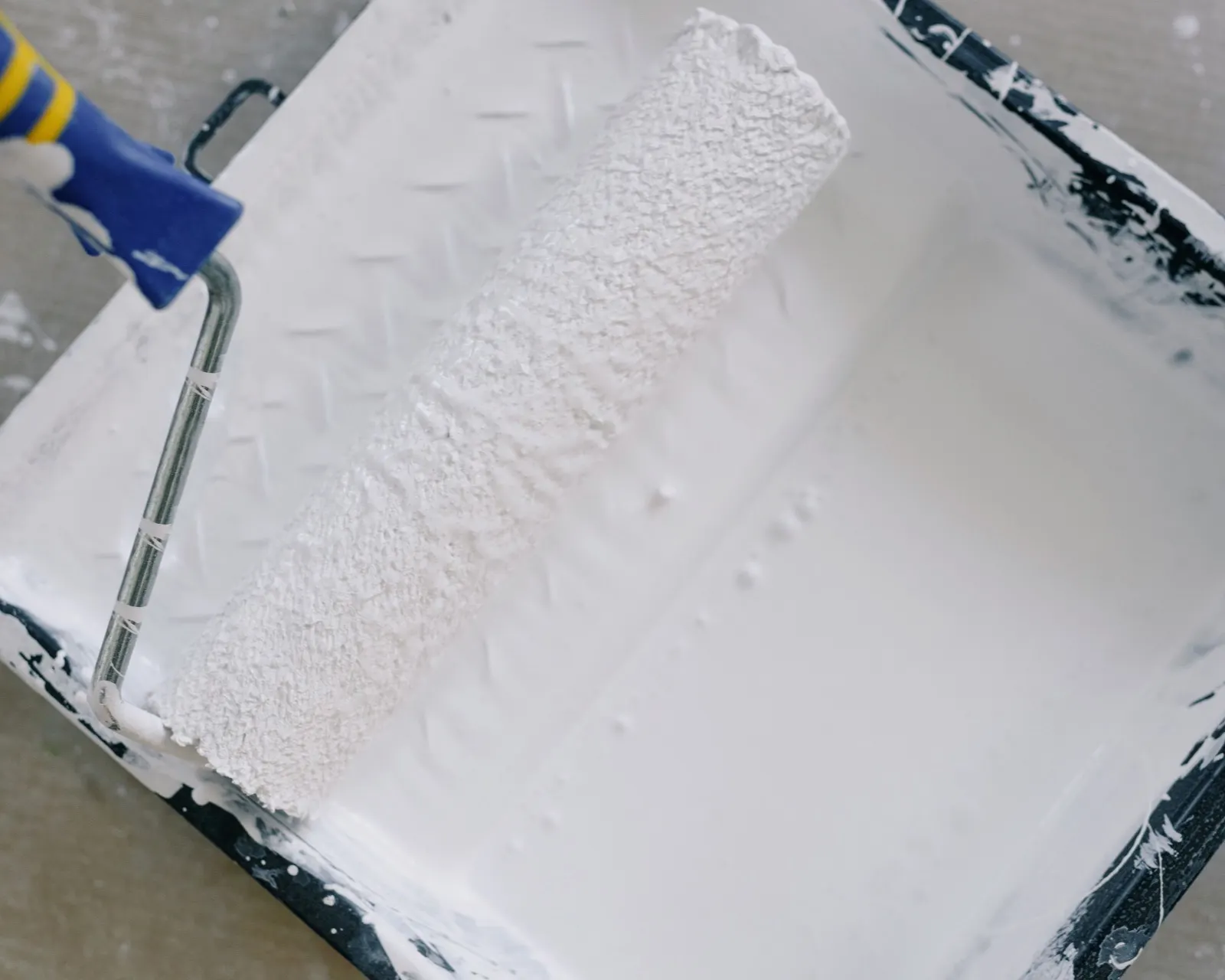 A paint roller resting in a tray of white primer