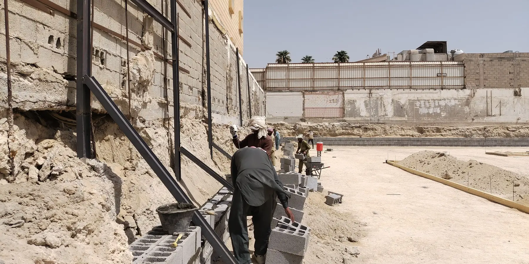 Workers laying concrete blocks for a retaining wall against a cut bank