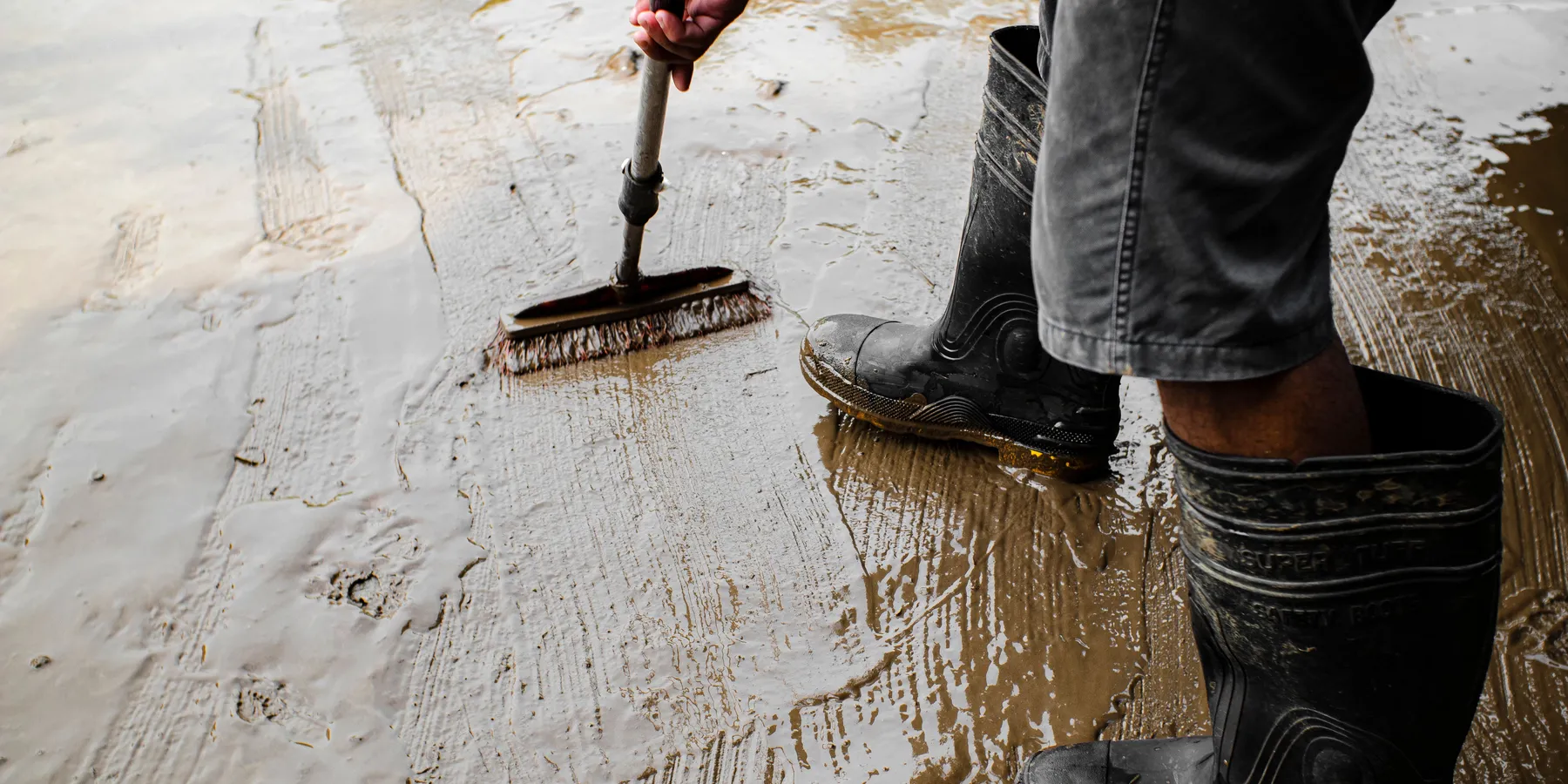 A worker in rubber boots brushing primer onto a concrete floor