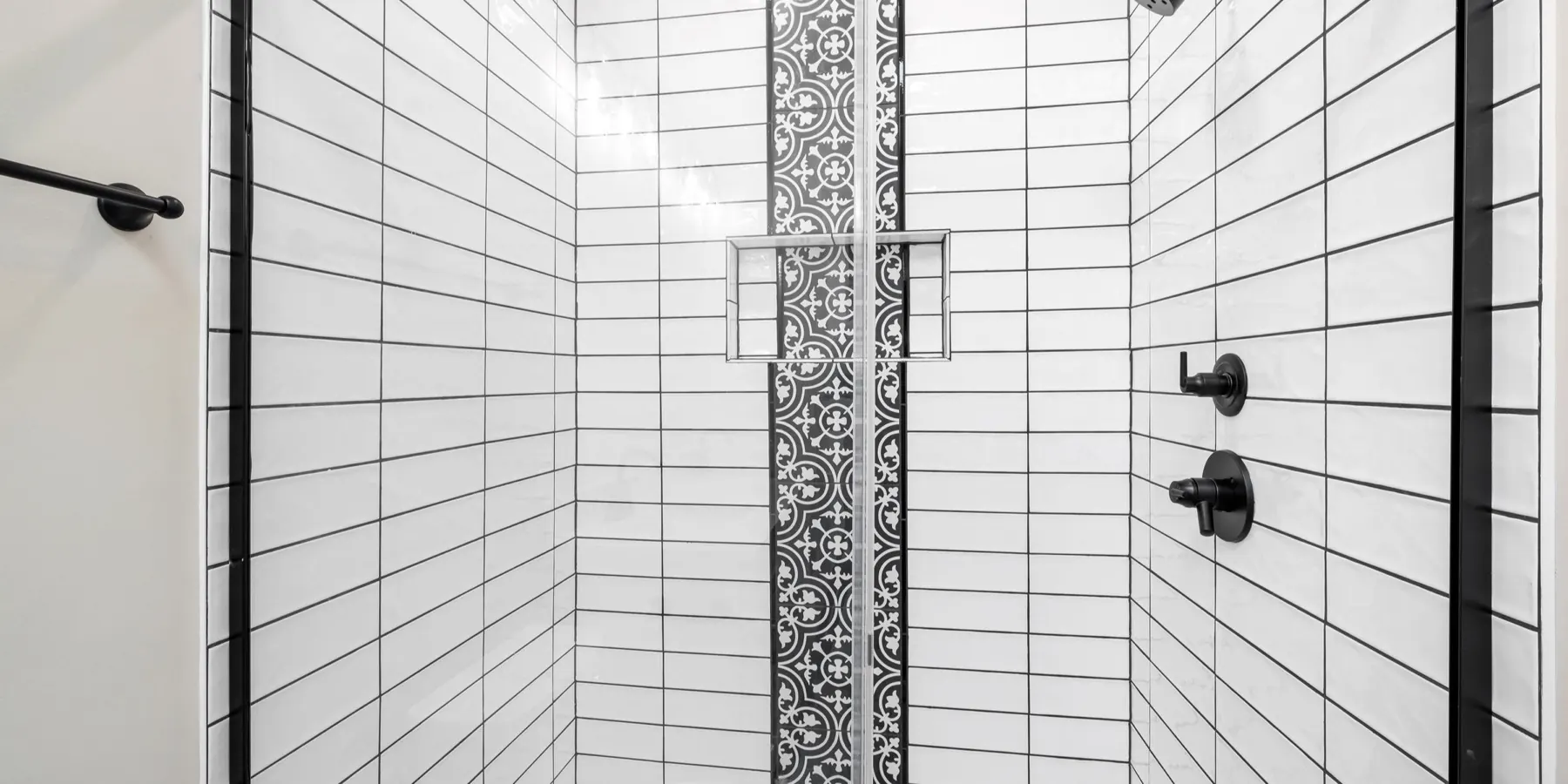 Tiled shower with white subway tile, black grout lines, a patterned accent strip, a recessed niche and a sliding glass door