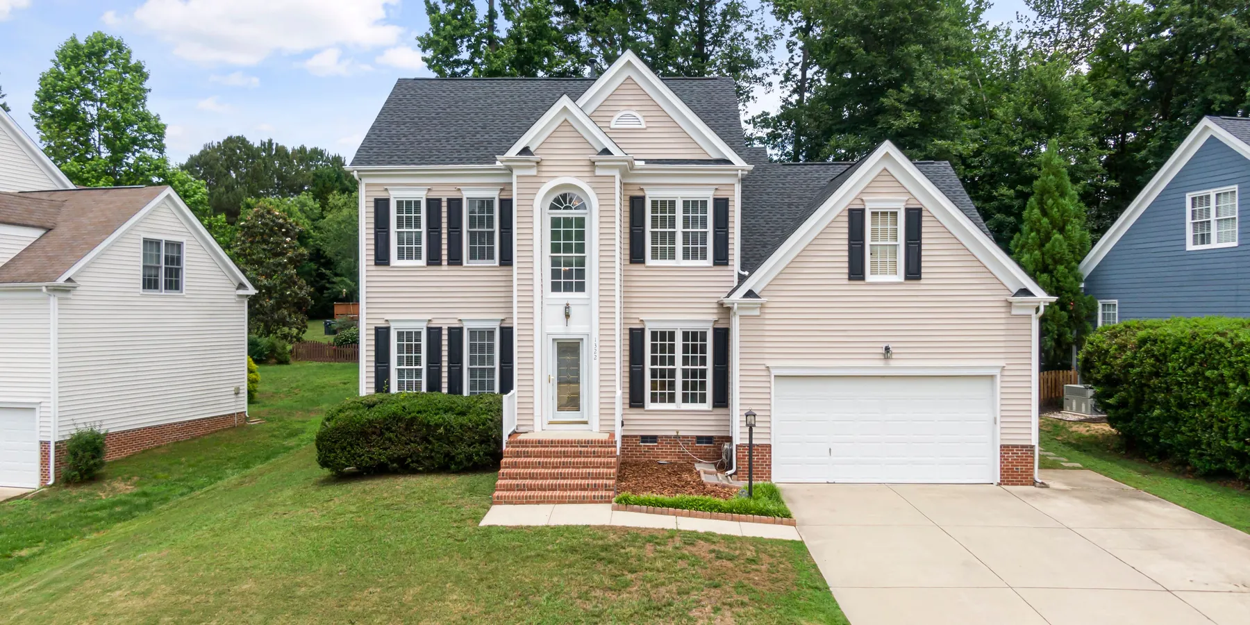 Two-story suburban house with cream vinyl siding, white trim, dark shutters and a two-car garage