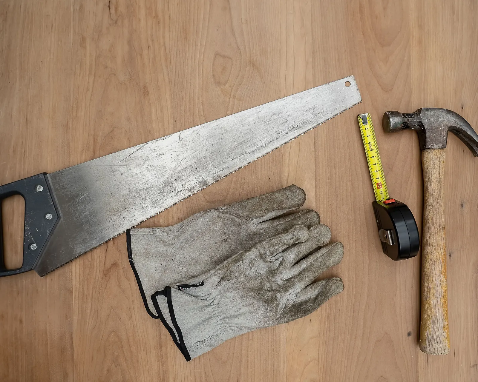 Hand saw, work gloves, tape measure and claw hammer laid out on a wooden bench, the basic kit for hanging siding
