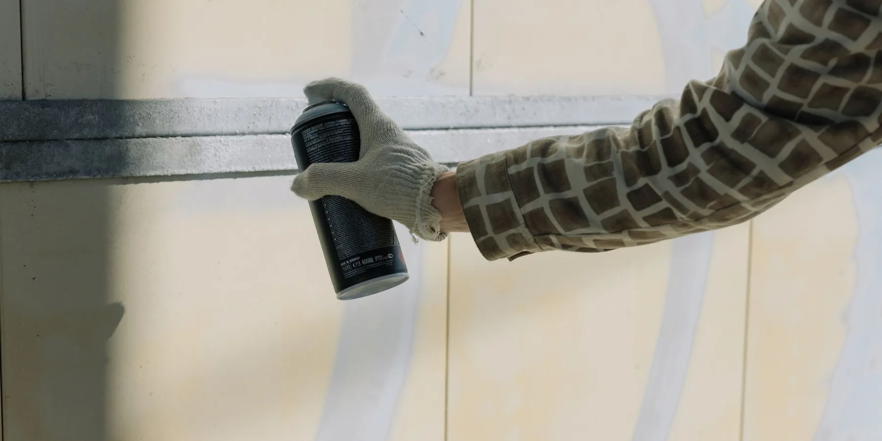 Gloved hand holding a spray paint can against a wall
