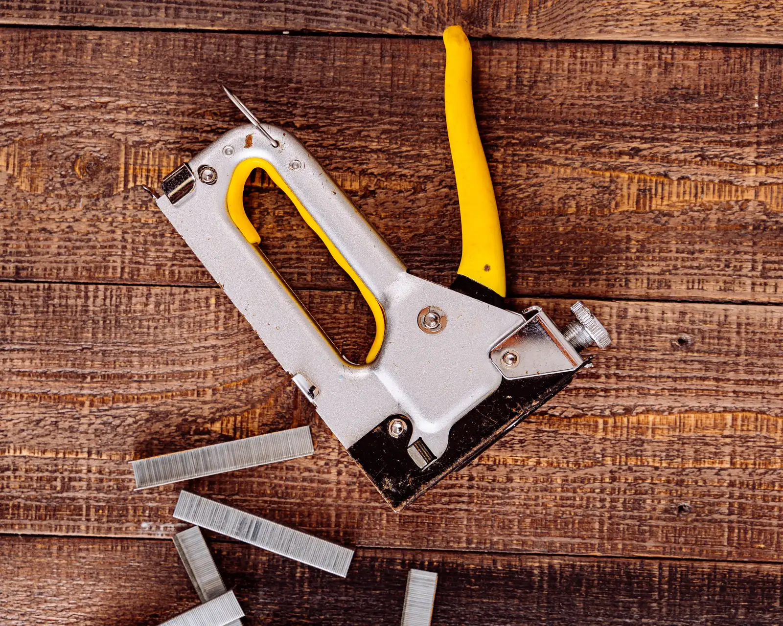 Staple gun with a yellow handle and loose staples on dark wood boards