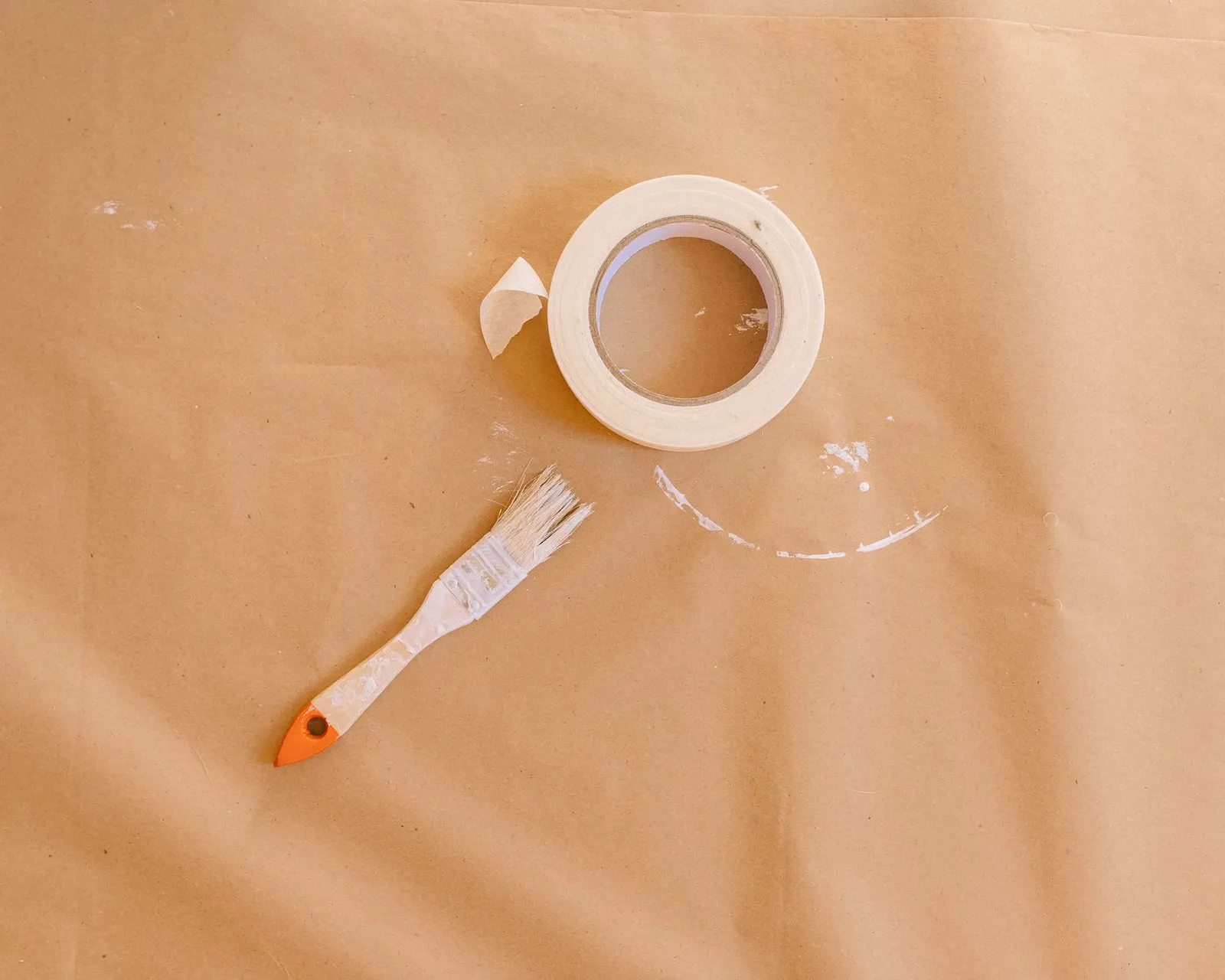 A small paintbrush and a roll of masking tape on brown paper